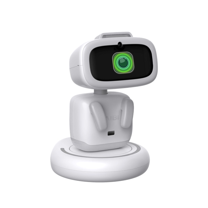 White AIBI pocket robot standing on its round charging base, its dark screen face showing a glowing green camera-lens icon.