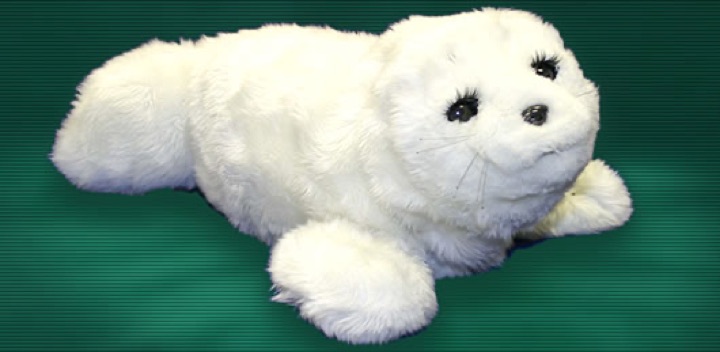 The white furry PARO therapeutic seal robot lying down with black eyes and whiskers on a dark green background.